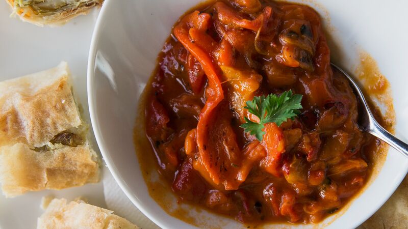 A bowl of Ajvar made with red bell peppers and eggplant. It looks like a salsa with a side of flaky bread. 