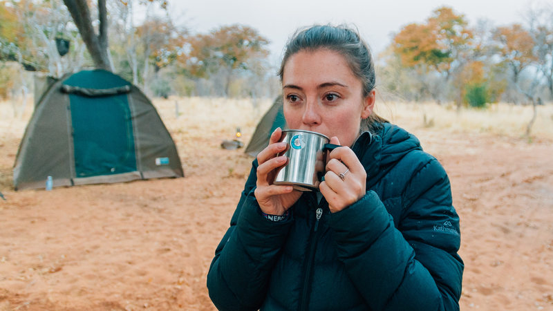 Woman sipping tea while in a warm jacket at a campsite in Africa