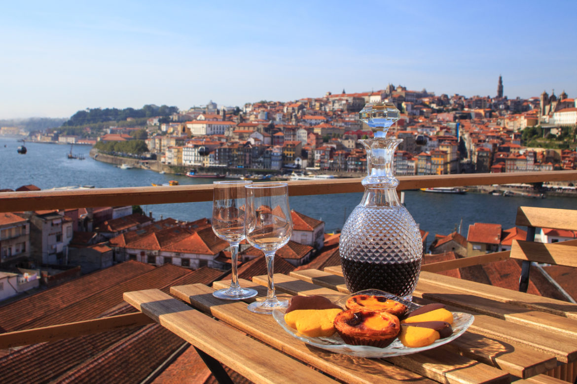 A decanter of wine and glasses sites on a table overlooking a river and town in Portugal
