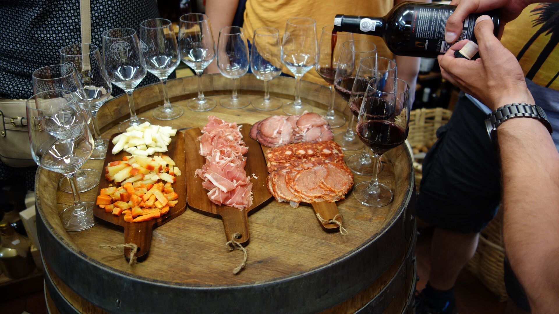 A man pours Port wine with a spread of local cheeses and meats next to the glasses