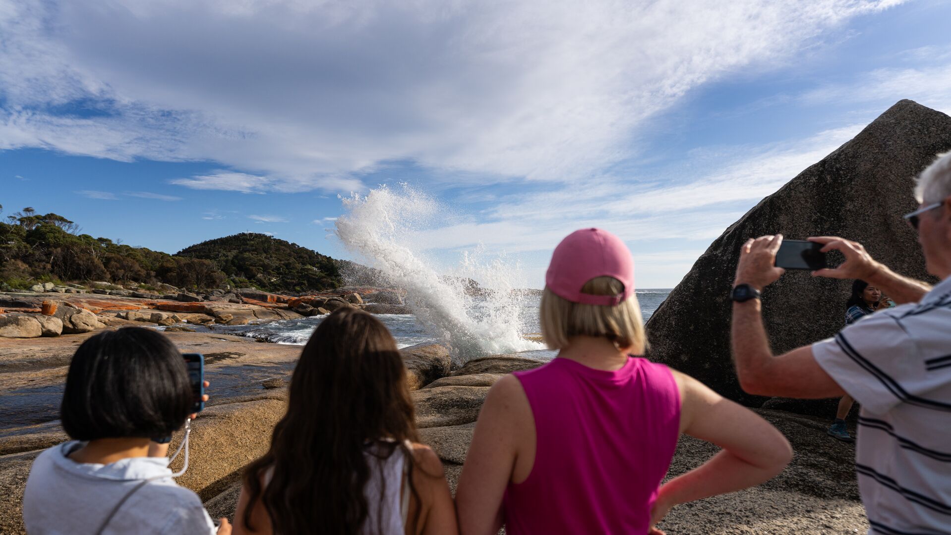 The Bicheno Blowhole erupting with water with four people watching on.