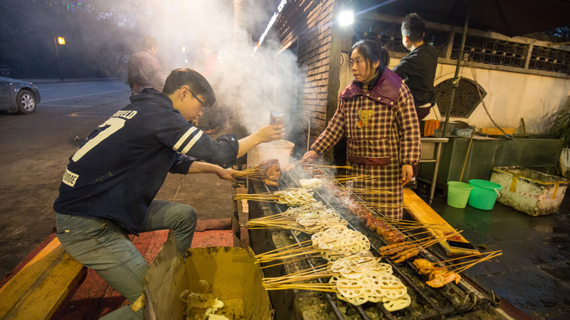Vendors grill sizzling skewers at a street food stall in China. 