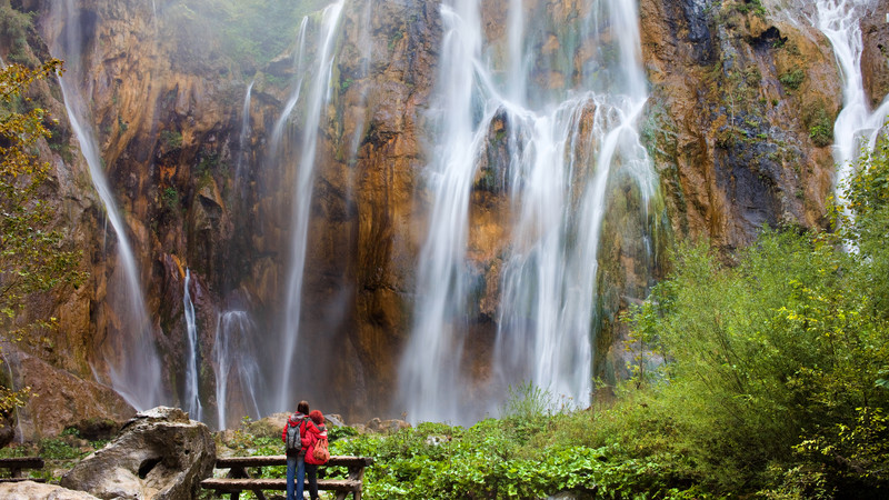 A couple stand in front of a waterfall in Plitvice Lakes