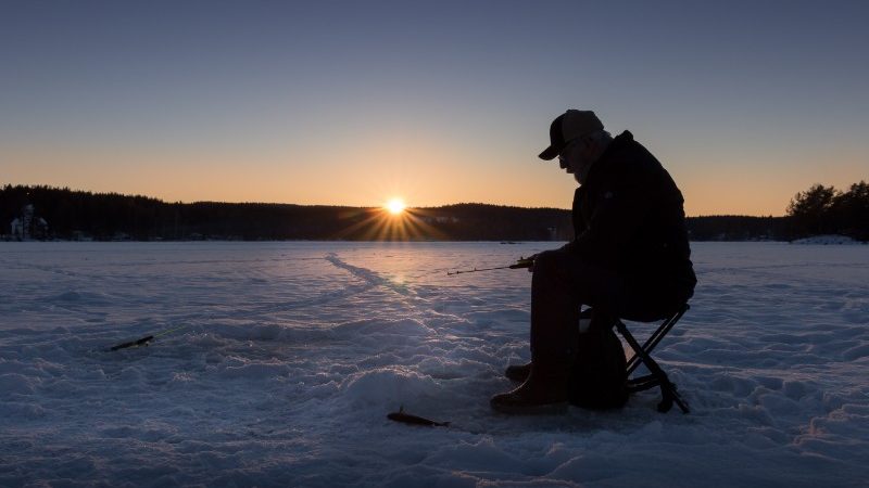 A fisherman sits on the ice waiting to catch a fish in Norway