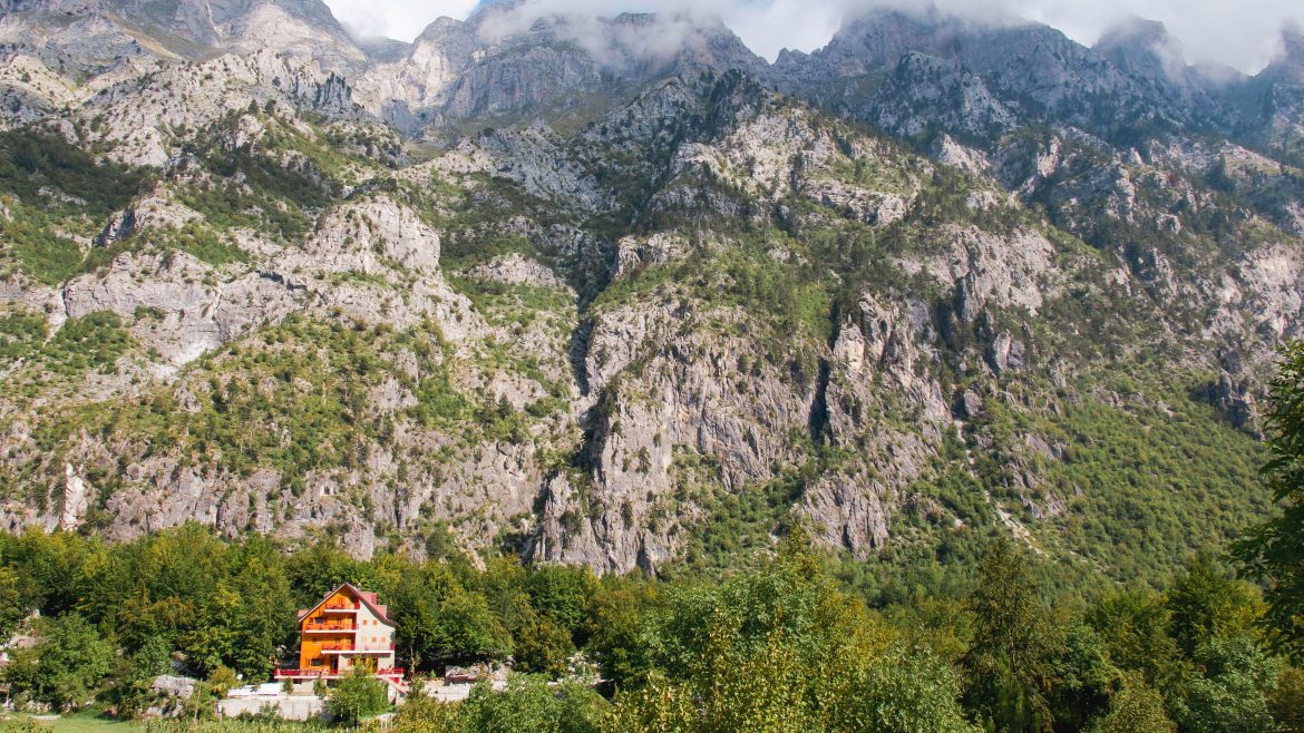 A house at the bottom of a tall rocky cliff in Valbona Valley, northern Albania