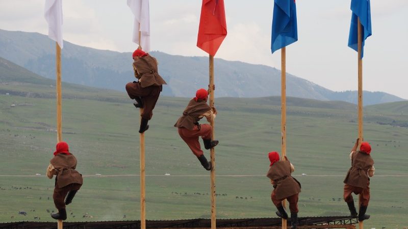 Five competitors climb flagpoles at the World Nomad Games