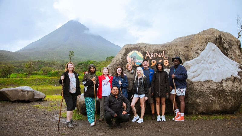 A group of ten Intrepid travellers dressed in hiking gear pose in front of Costa Rica's Arenal Volcano.