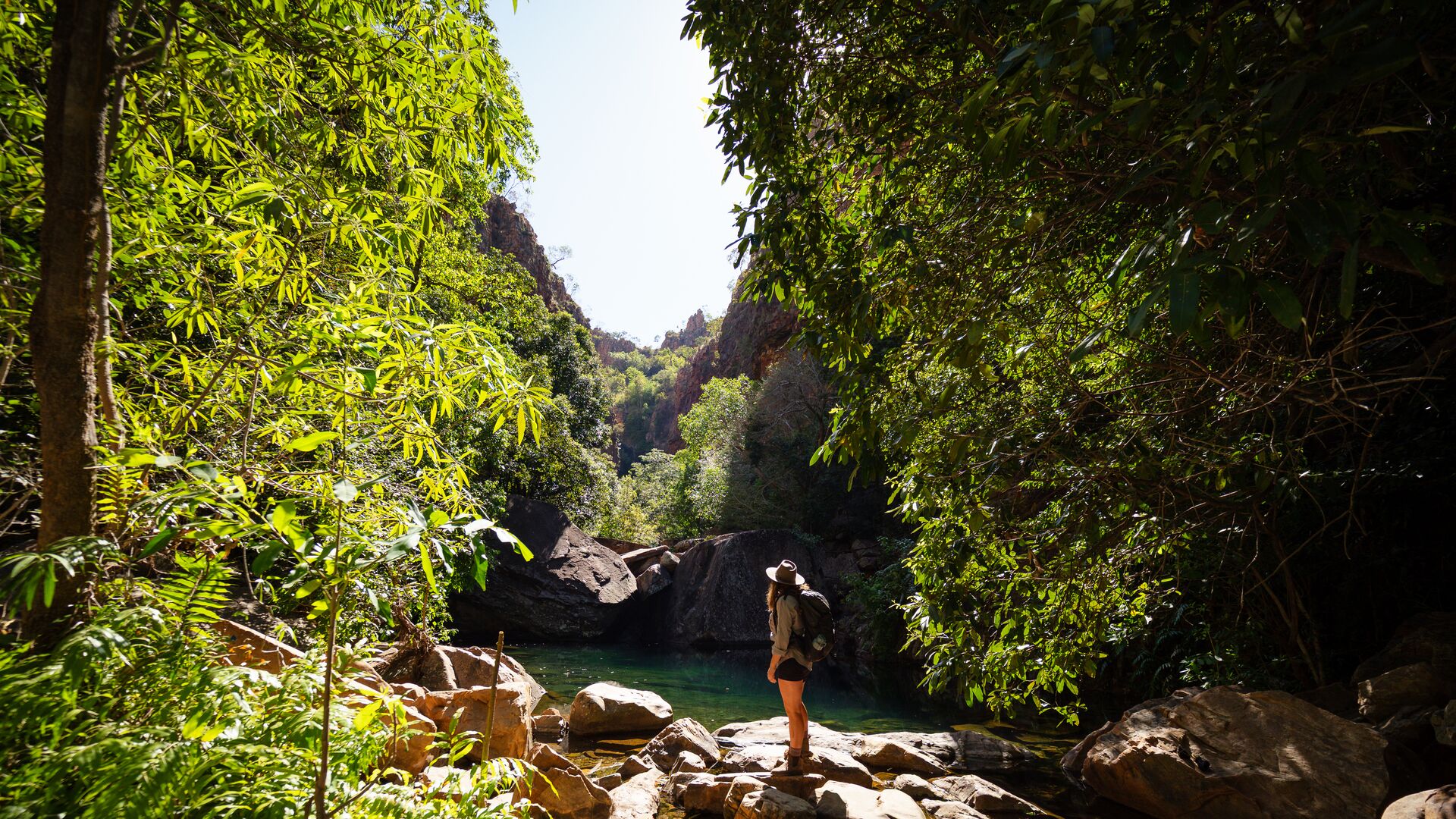 A woman stands on rocks looking out at a pool in the Kimberley's El Questro region.