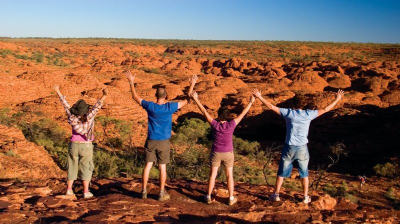 A group of travellers standing at the top of Kings Canyon with their arms out wide 