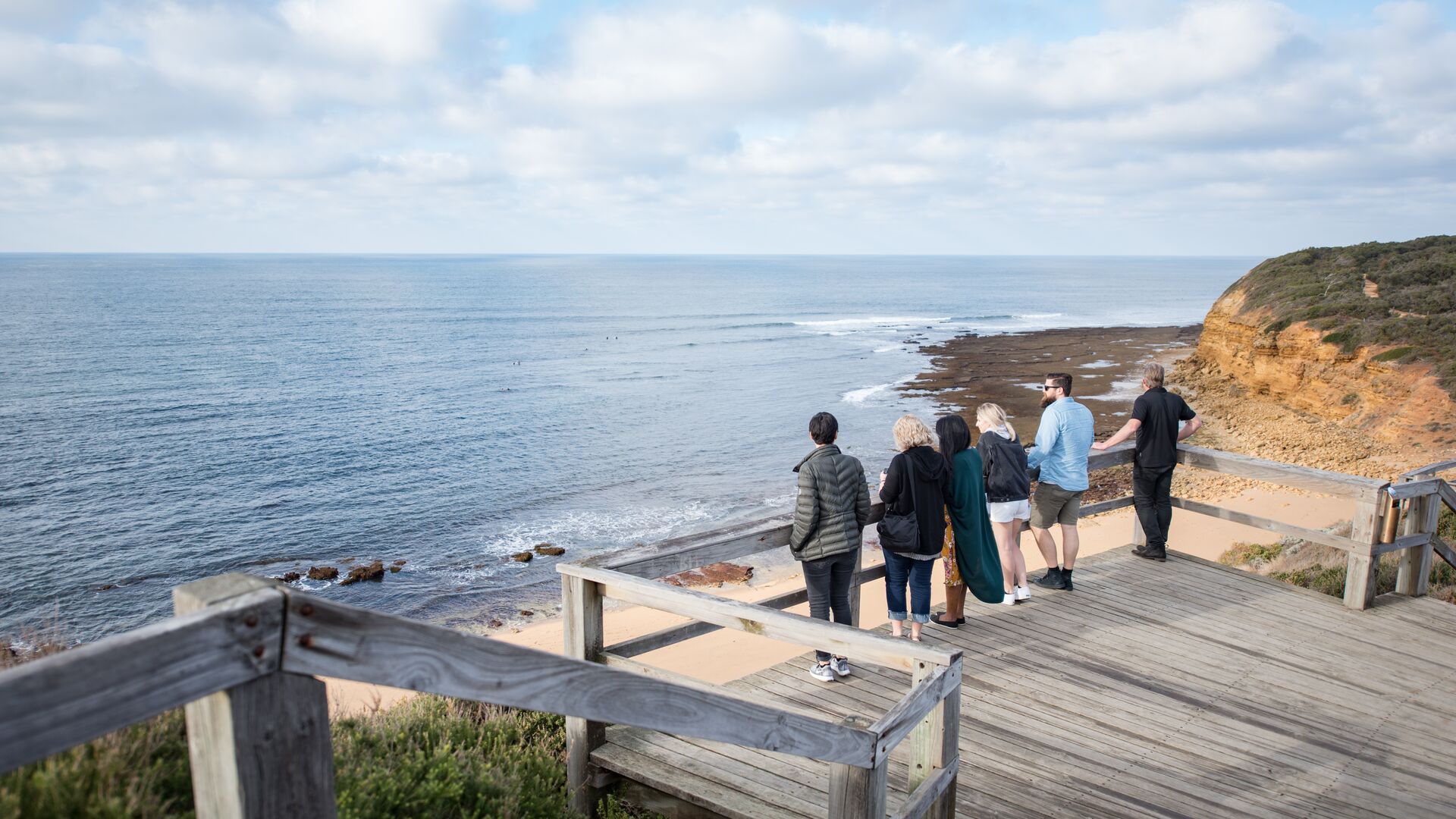 Six people stand at a lookout over Bells Beach on the Great Ocean Road.