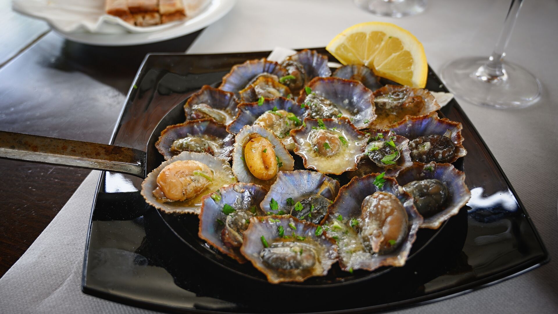 A plate of seafood limpets in butter sauce - it looks like open mussel shells covered in butter with a lemon wedge on a table. 