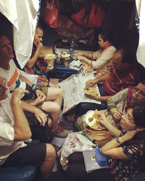 A full seating area of a train with local people and travellers talking and sharing a meal