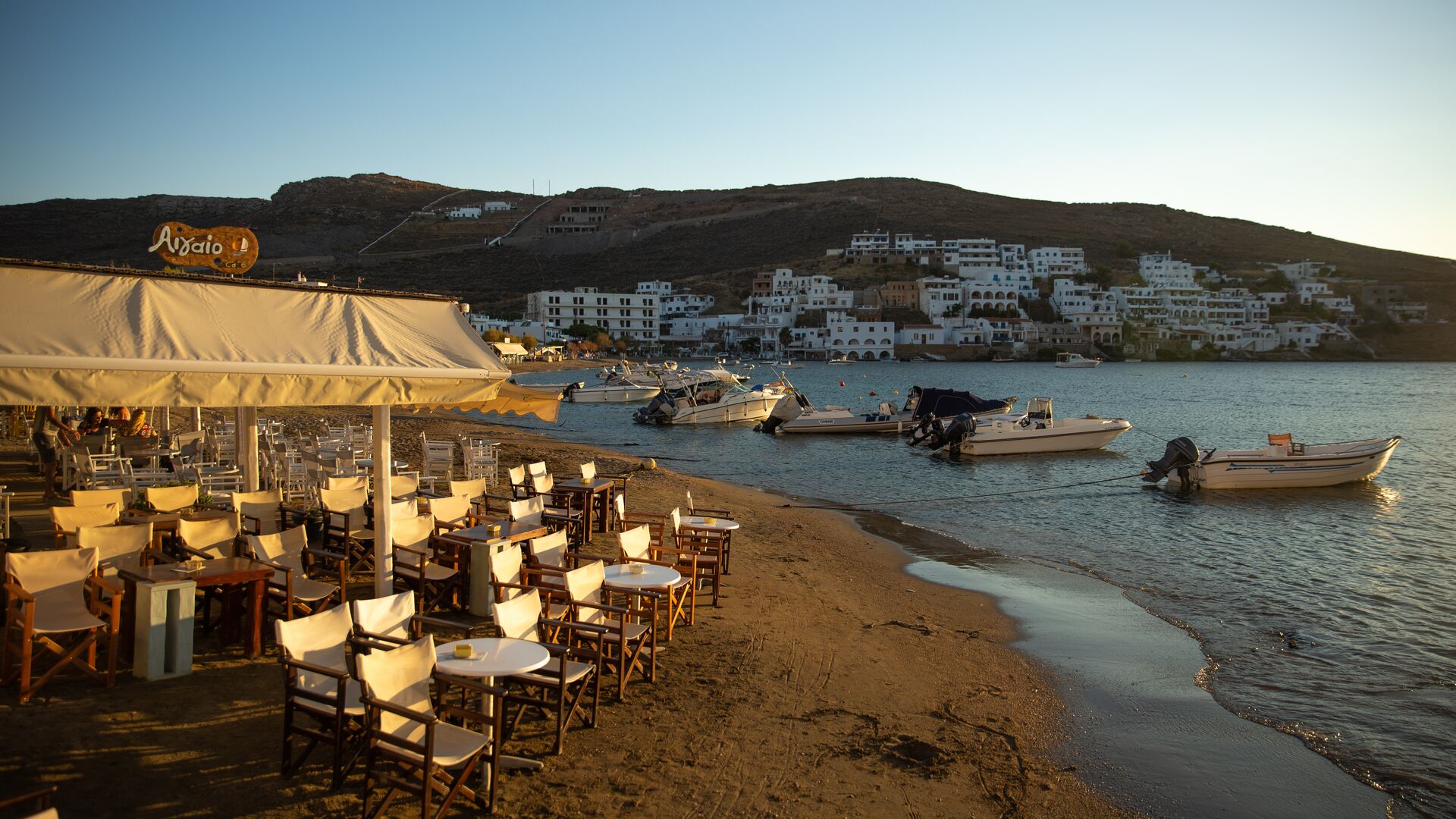 Tables and chairs at a beachside restaurant at golden hour in Kythnos, Greece