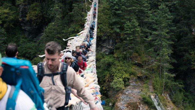 Group of travellers walking along a suspended bridge to Everest Base Camp though forests and shrubs