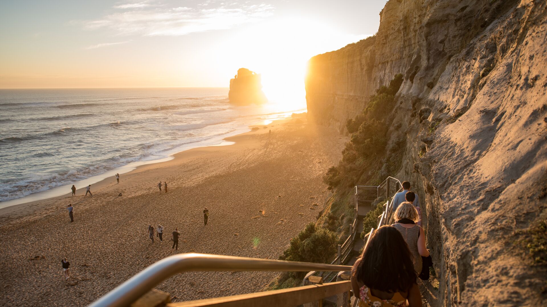 A group of people descend the Gibson Steps while others walk on the beach at sunset.