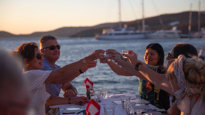 A group of travellers cheers their drinks at sunset.