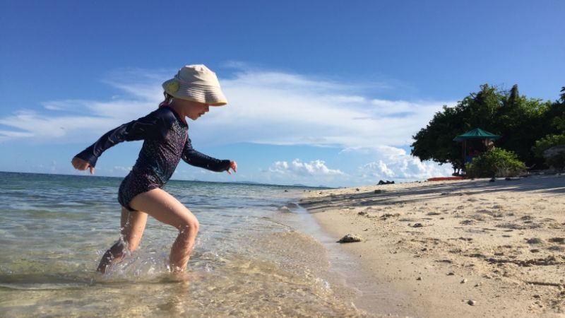 A little girl in a hat playing at the beach