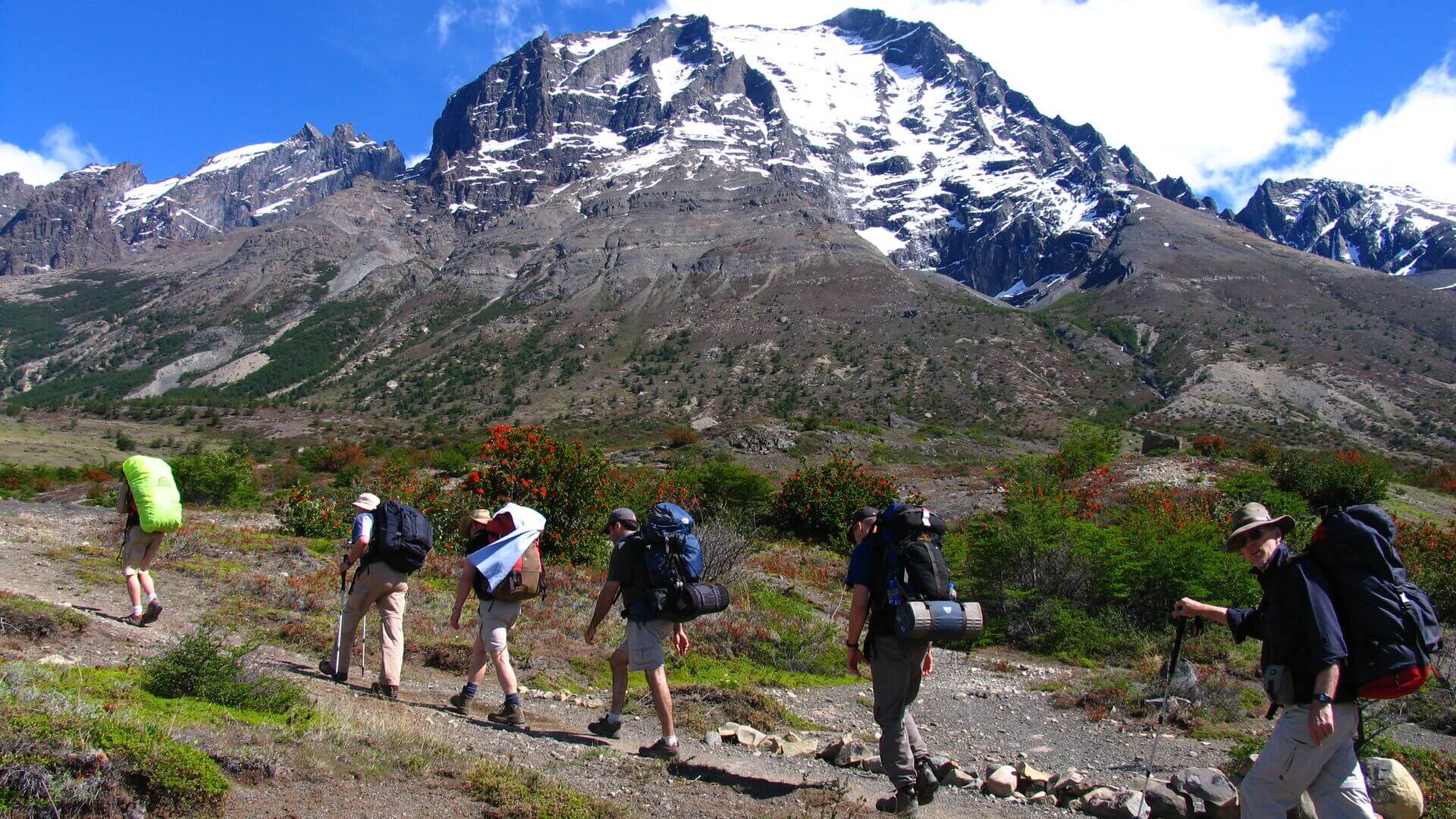 A line of hikers on a trail passing the snowy peaks of Torres del Paine National Park, Chile