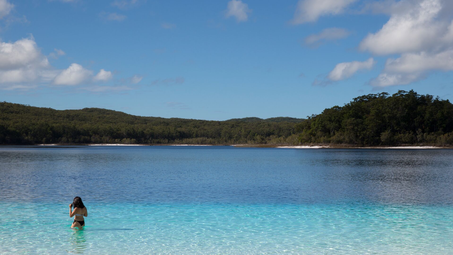 A woman stands in the waters of Lake McKenzie on K'gari.