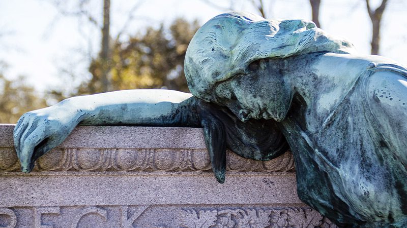 A statue of a women laying over a tombstone at Metairie Cemetery in New Orleans.