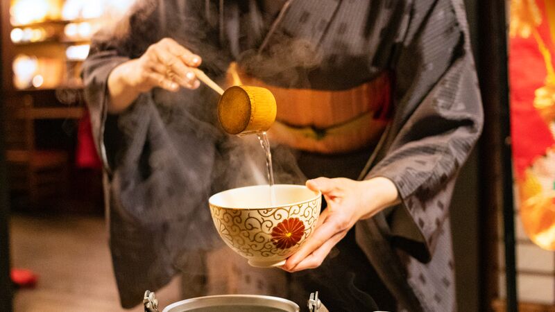 Traditional Japanese tea master ladling green tea into a bowl.