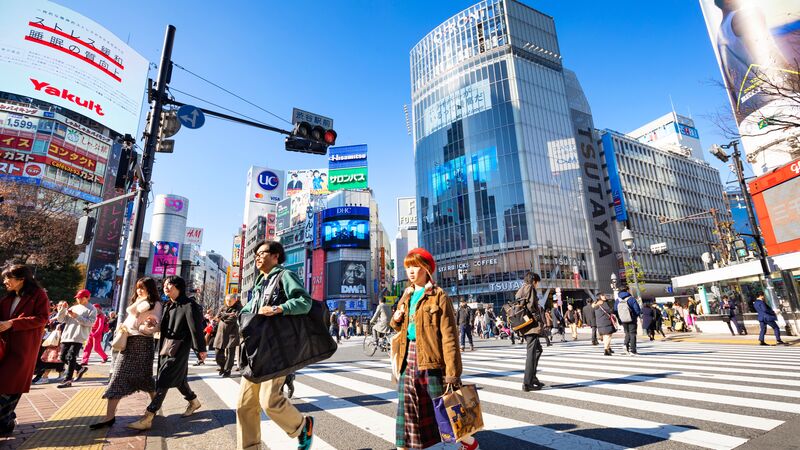 People walking hurriedly across Shibuya Crossing with skyrise buildings in the background.