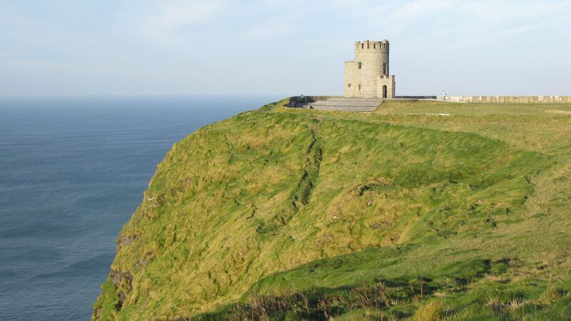 A castle stands on the green, grassy edge of the Cliffs of Moher.