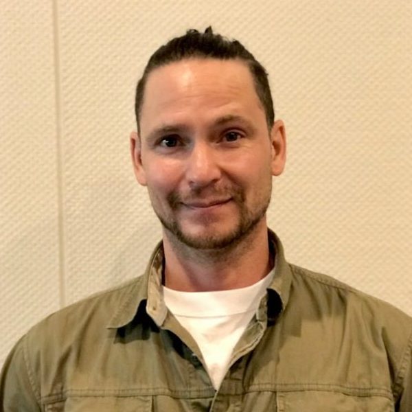 A man wearing a khaki-coloured shirt smiles at the camera