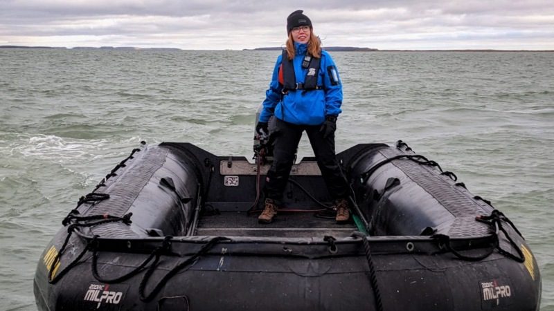 A woman wearing a beanie and blue jacket standing on an inflatable boat in the Antarctic