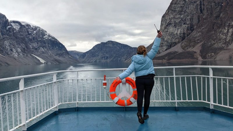 A woman standing on the bow of a ship with her arms in the air
