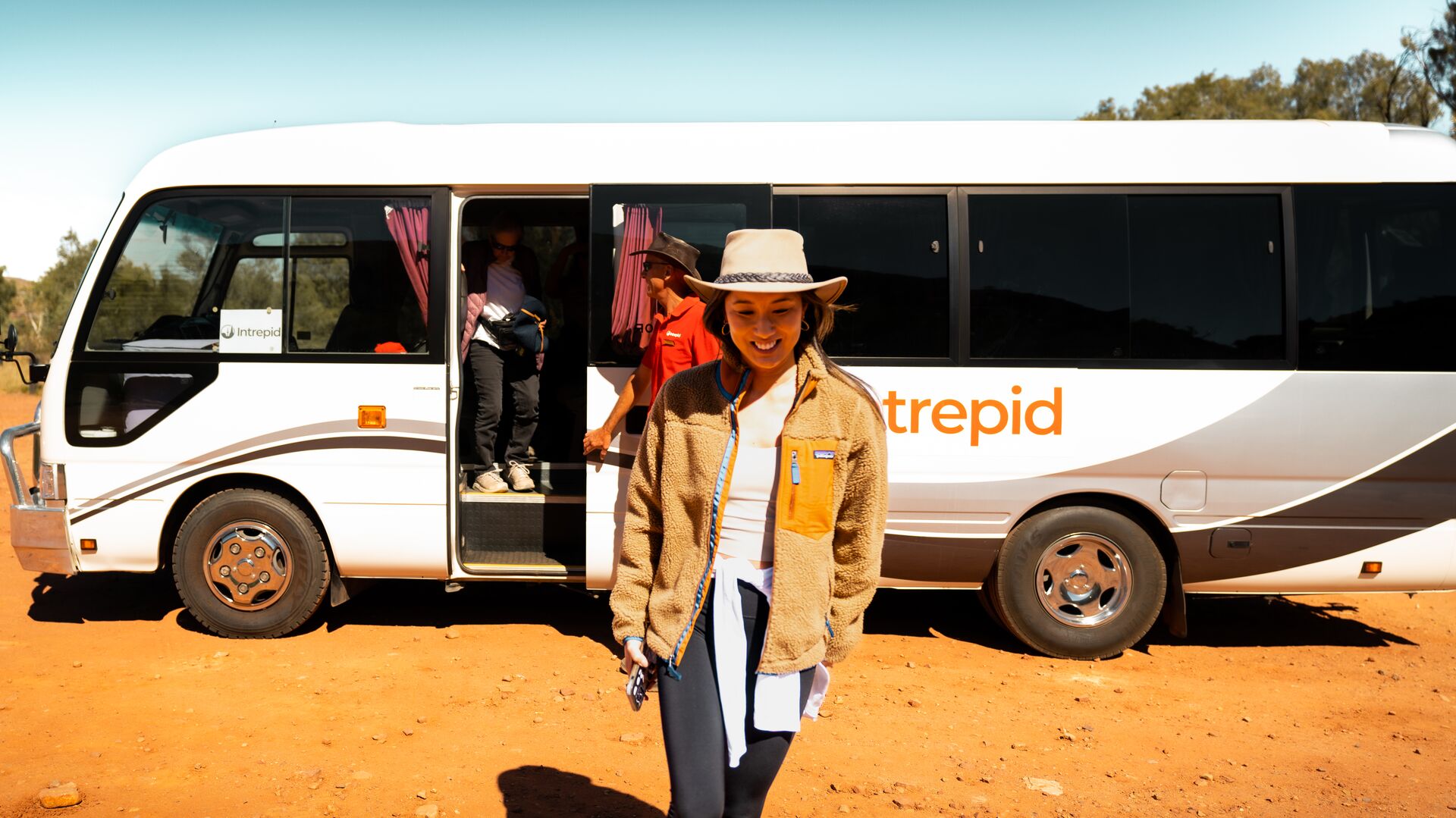 Travel influencer, Sarah, walks out of Intrepid bus on red dirt road.