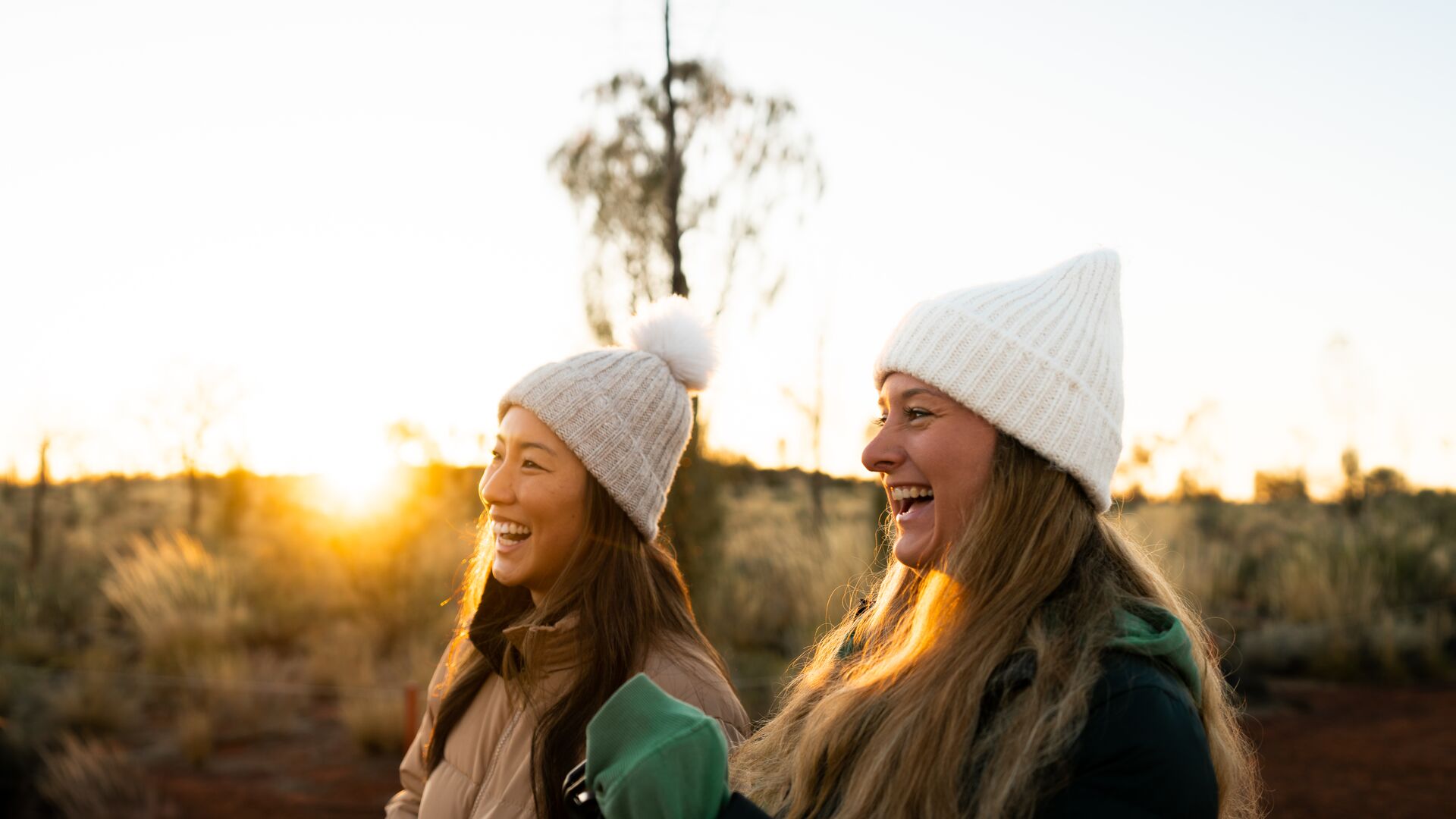 Two travellers smiling as they look out at Uluru at sunrise.