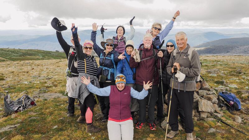 A group of travellers smiling at the camera, their arms in the air, with mountain range in the background.