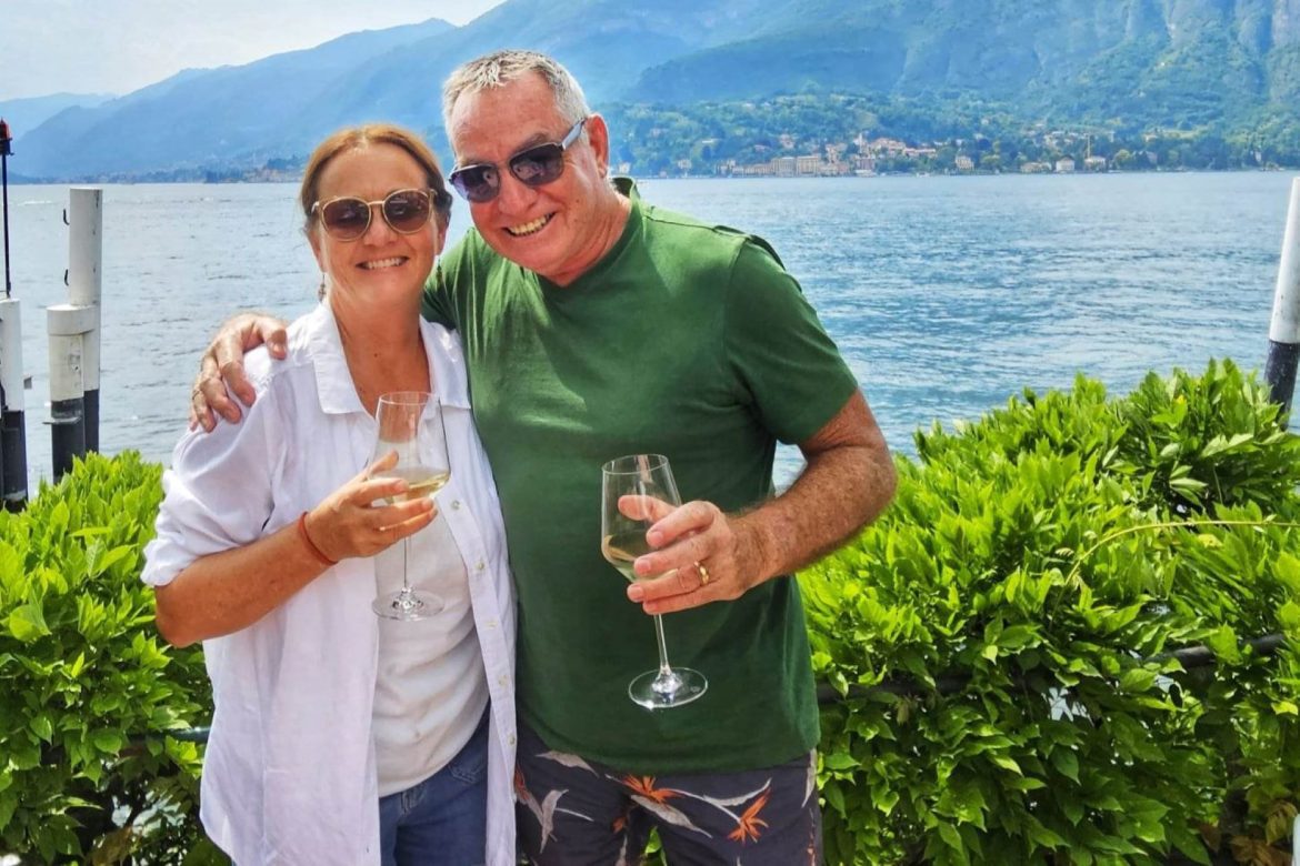 a man and woman by the lake holding wine glasses
