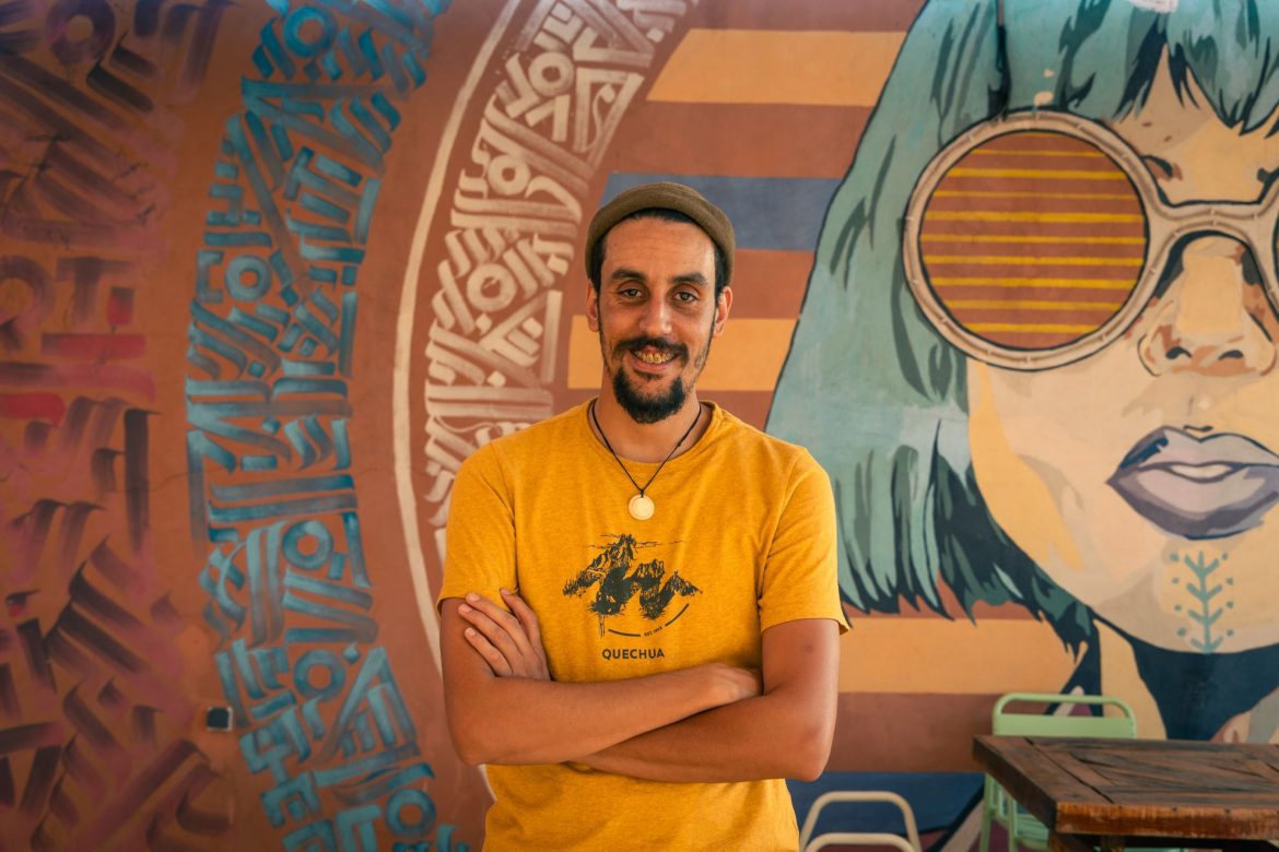 a man smiling in front of a piece of artwork of a woman wearing sunglasses