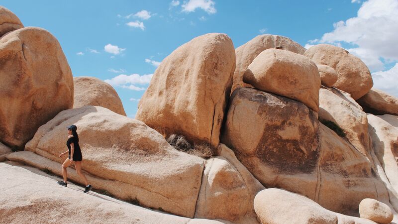 A traveller walks up a rust coloured stone formation in Joshua Tree National Park