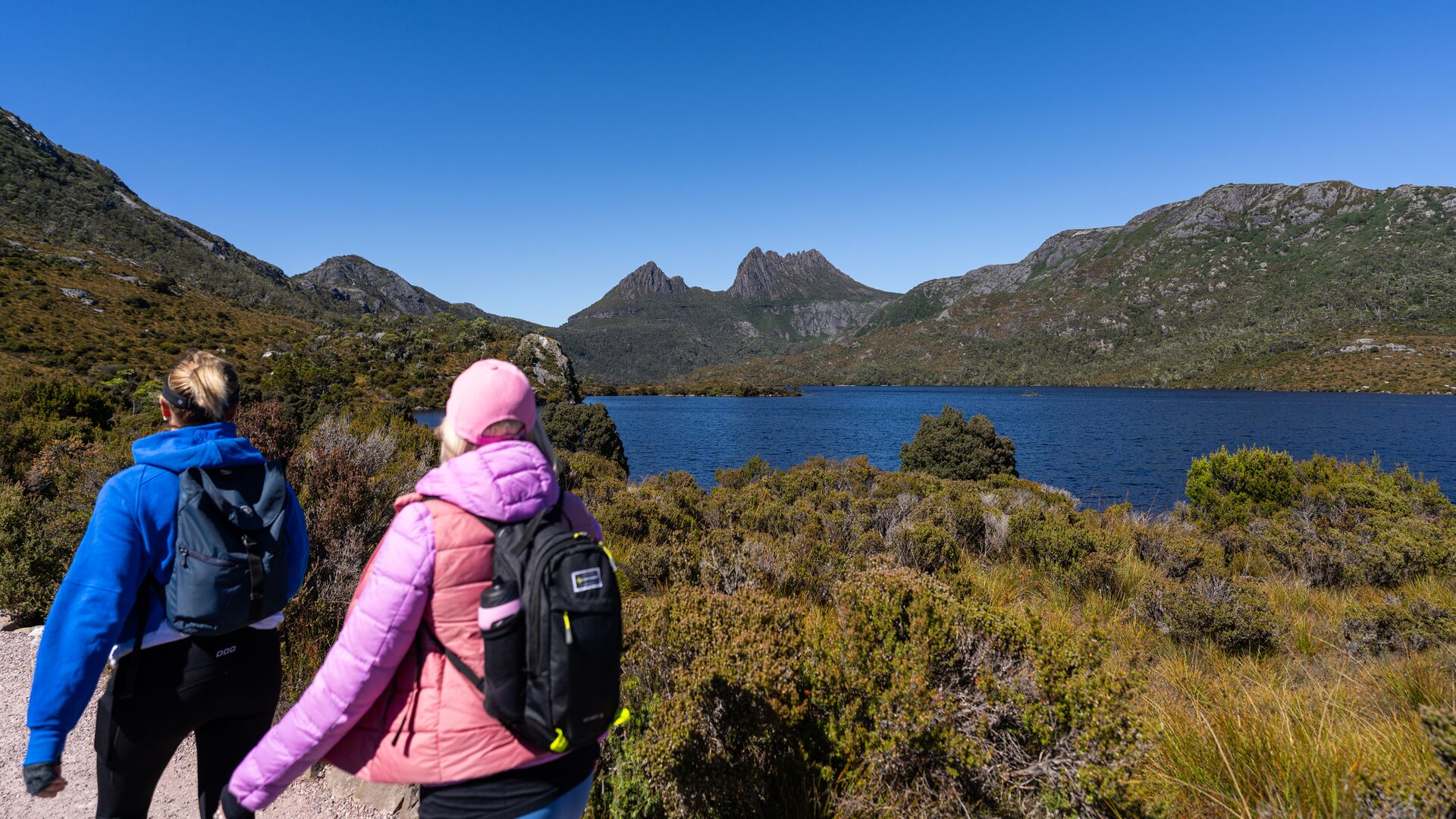 Two women hike past Dove Lake and Cradle Mountain.