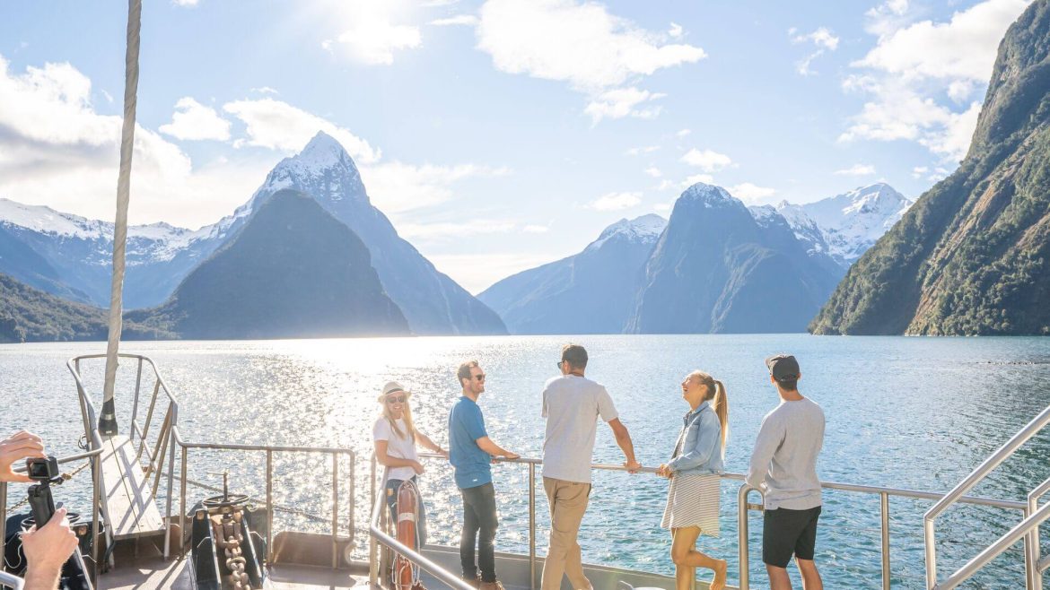 Group of five people smiling on a boat, looking out over the mountains of Milford Sound, New Zealand