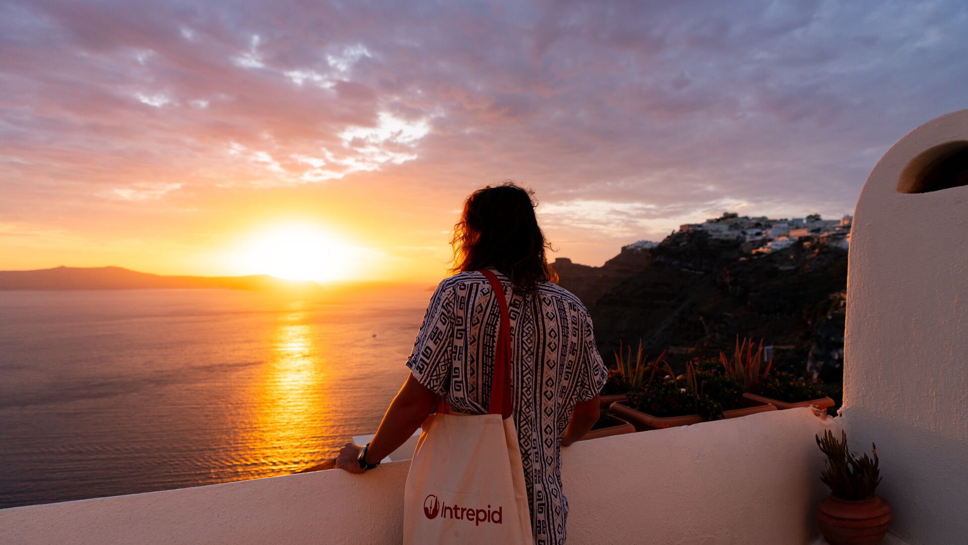 A traveller admires the sunset in Santorini, while carrying a classic Intrepid tote.