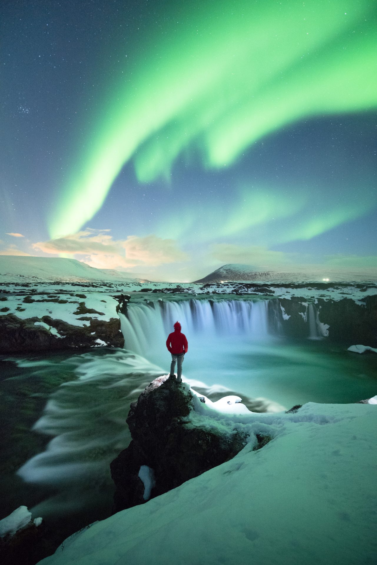 A traveller admnires the Northern Lights and a waterfall in Iceland