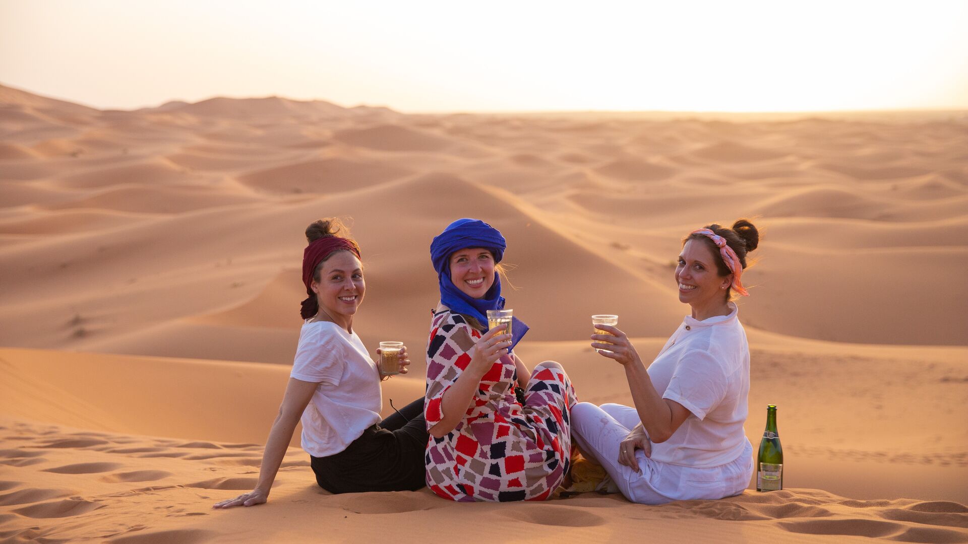 Three women raise a glass in the Sahara
