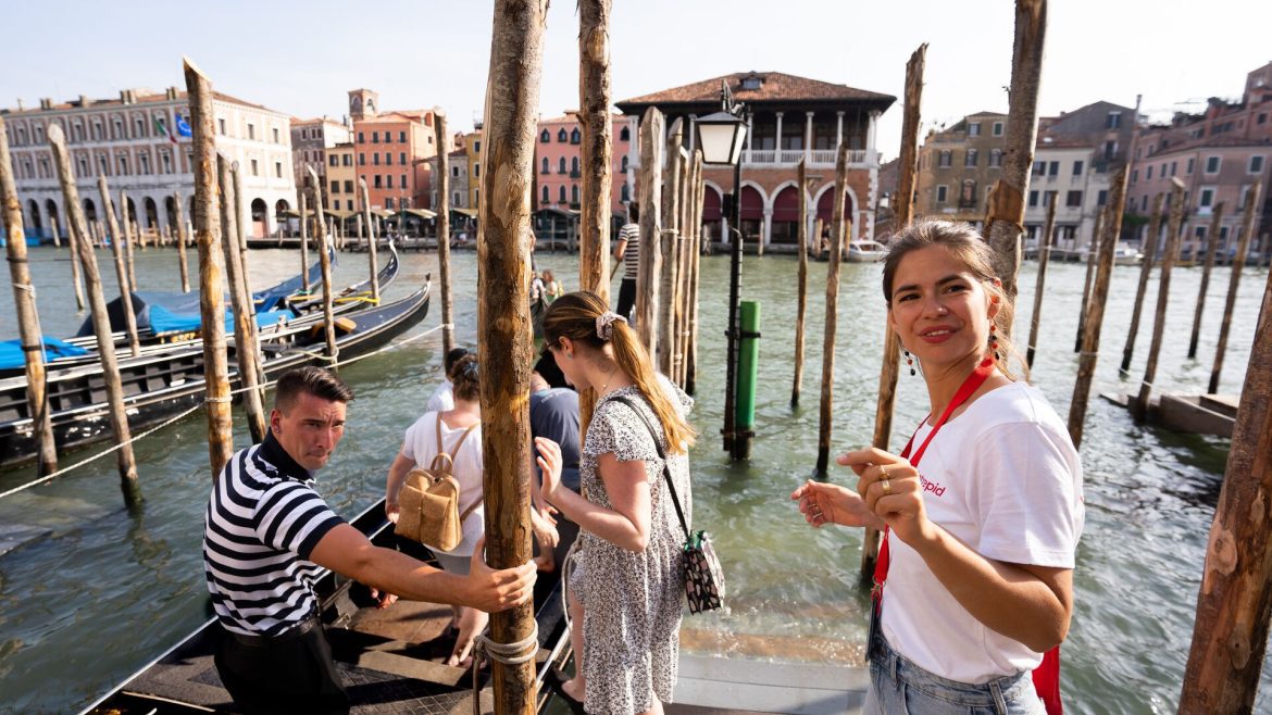 A tour leader in a white shirt guides travellers on to gondola in Venice, Italy.