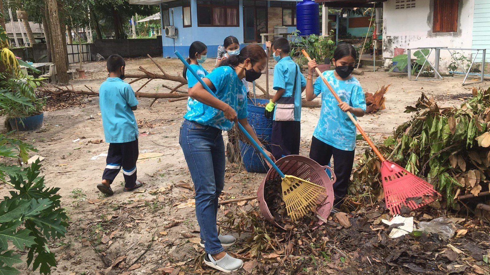 A group of kids and their teacher in Thailand sweep up a yard, hunting for litter.