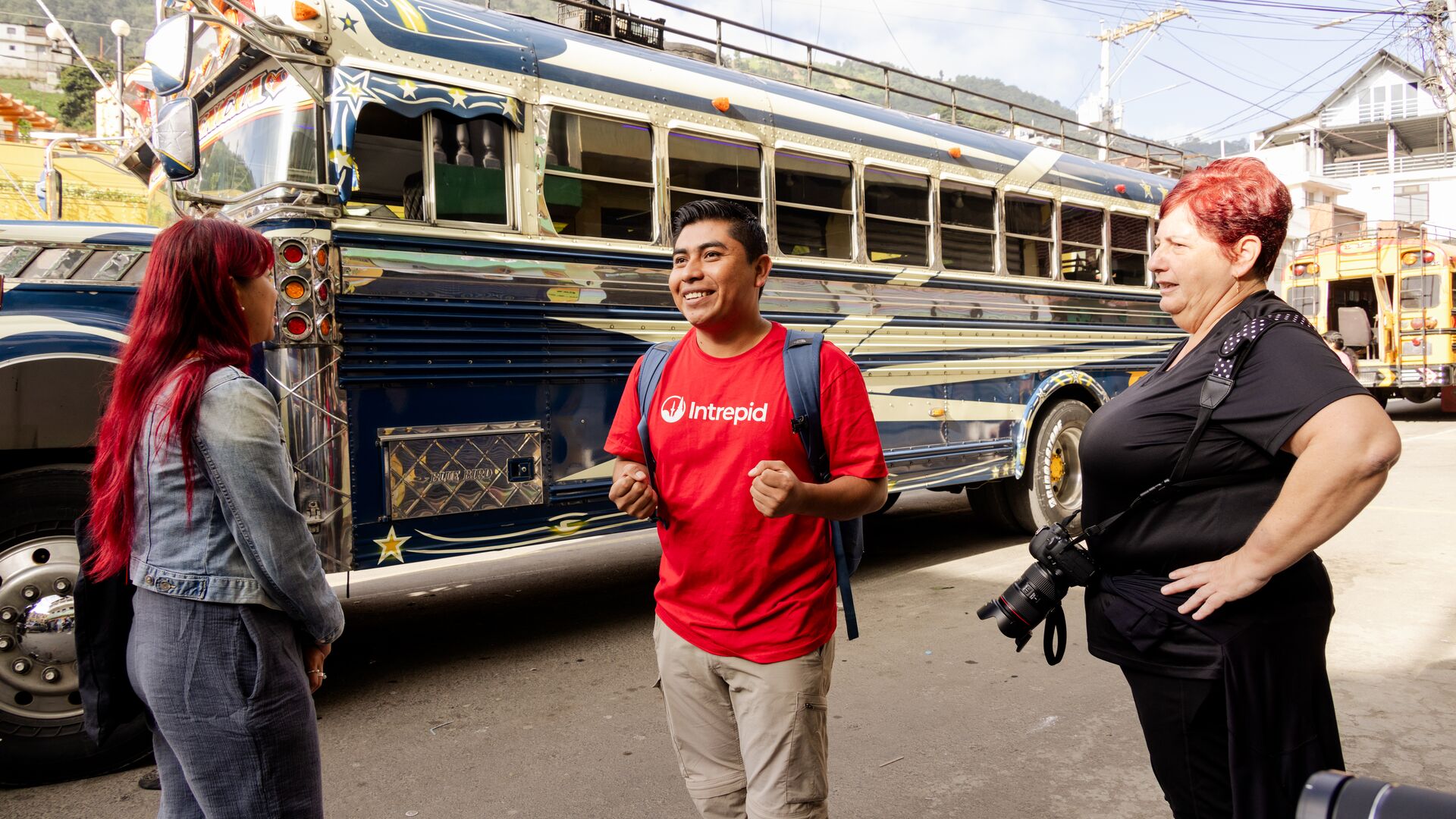 An Intrepid leader and two travellers chat in front of a chicken bus in Guatemala