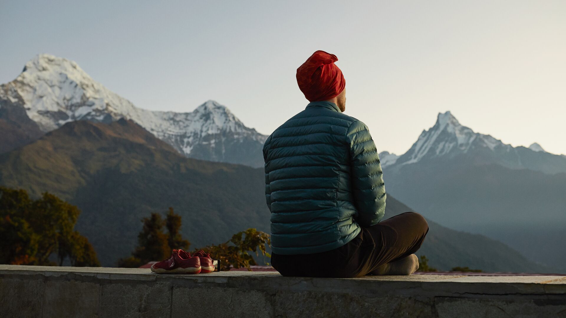 A man sits cross legged, taking a moment to soak up the mountain views at sunset in Nepal