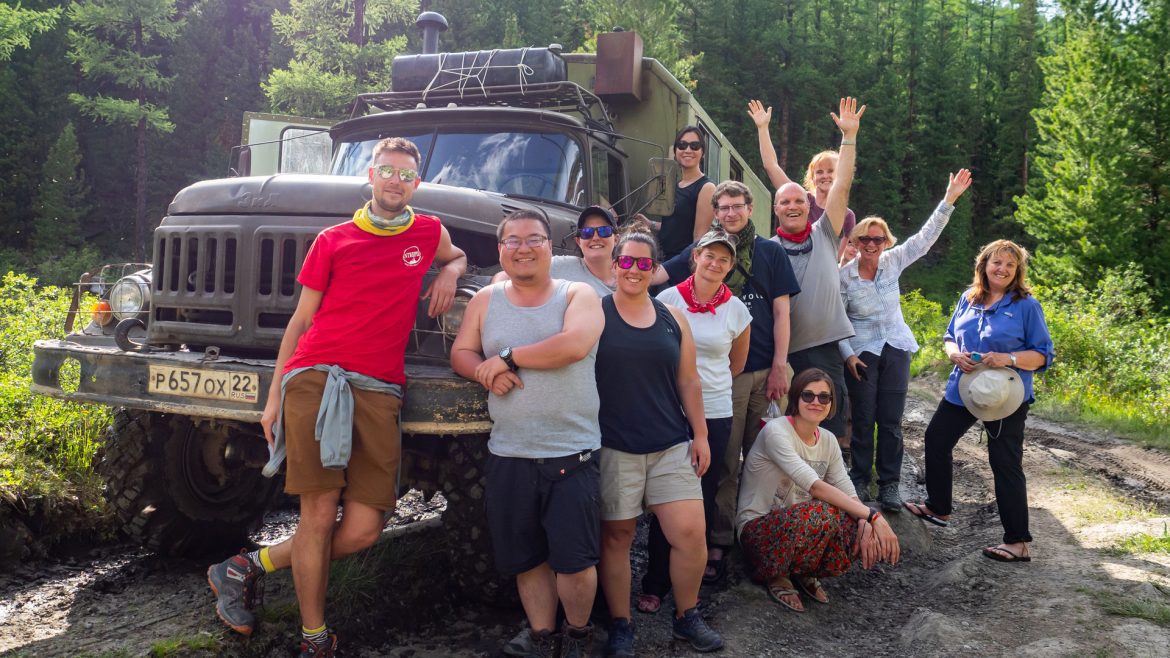 A group of Intrepid travellers on an Uncharted Expedition posing in for a group photo in front of an expedition vehicle.