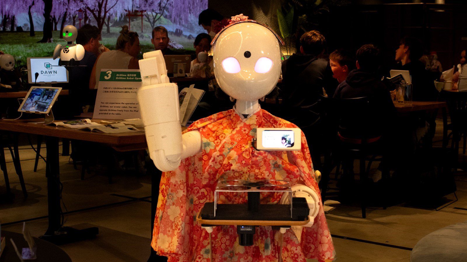 A life-size robot waves at the camera.