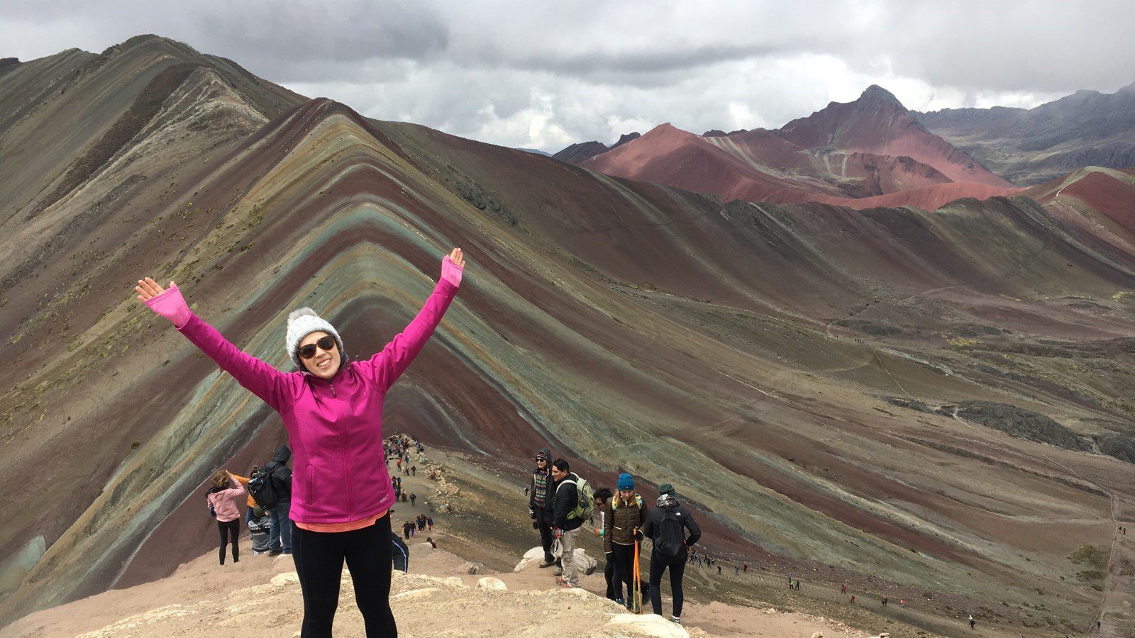 Writer Morwenna poses with her arms in the air, backdropped by Peru's rainbow mountain.