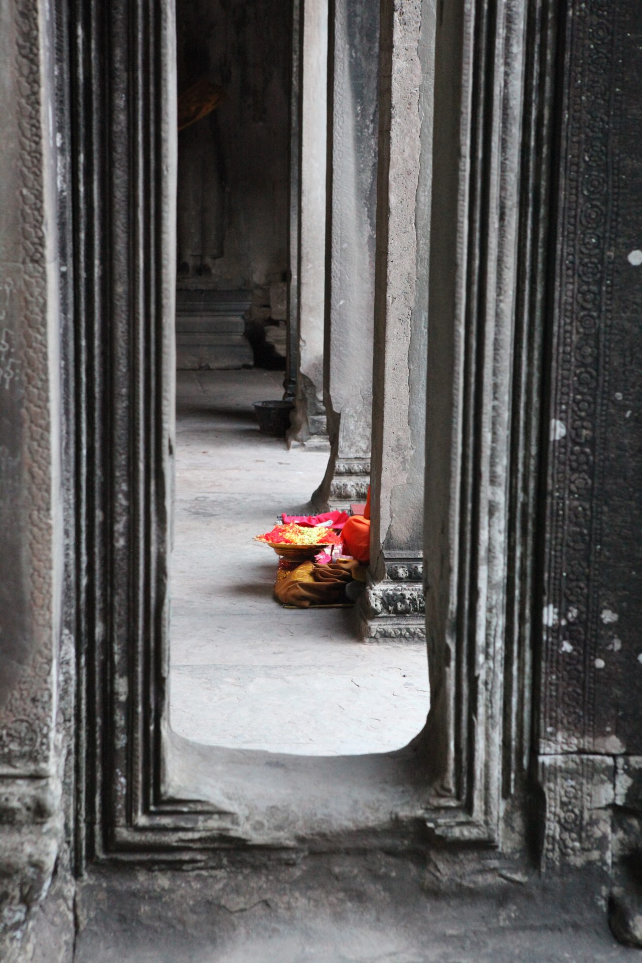 An orange-clad knee of a monk peeks out from behind a pillar at Angkor Wat