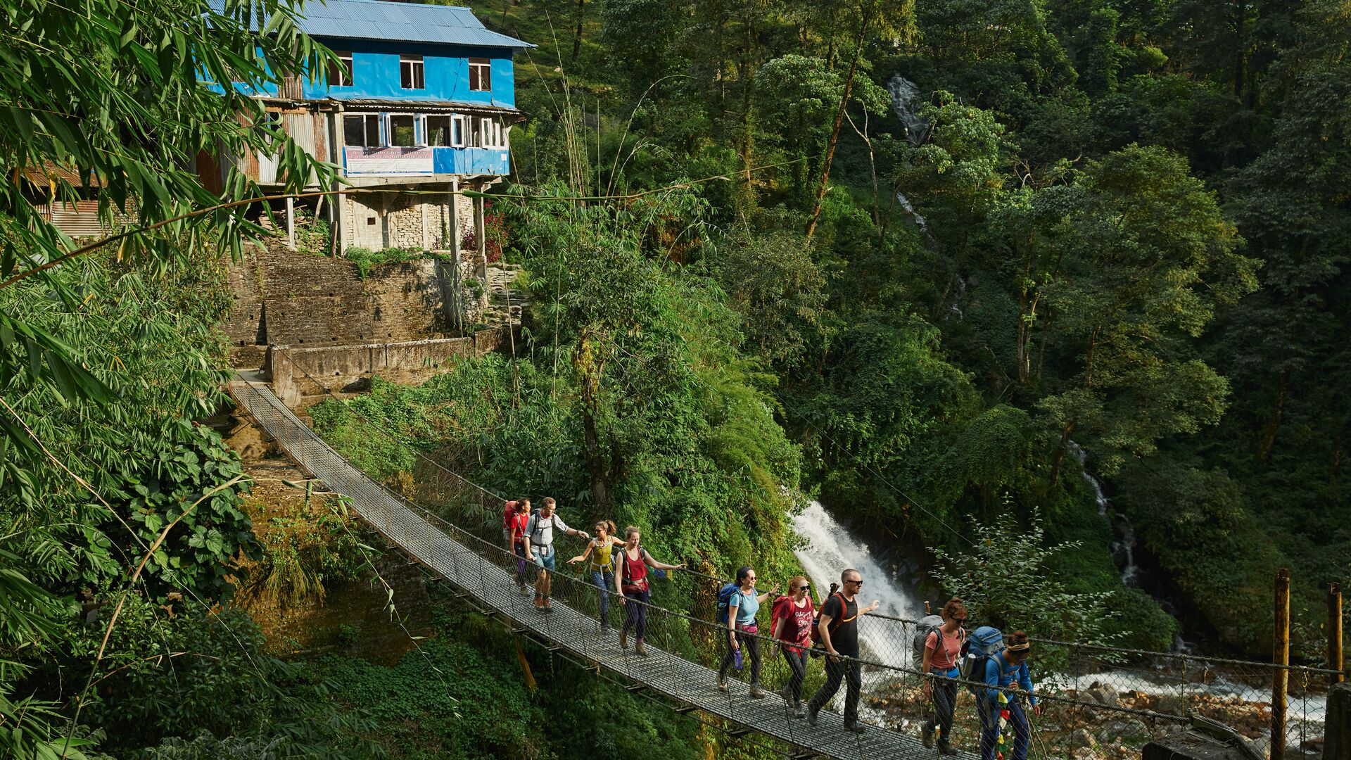 A group of travellers crosses a suspension bridge in the Himalayan foothills.